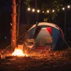 A campsite at night with a tent, campfire, and string lights. Anteprima dell’immagine prodotto