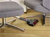 A cordless vacuum cleaner head is shown cleaning the floor between two grey upholstered ottomans. Produktbild-Vorschau