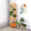 A wooden planter with a trellis is filled with plants and flowers, placed next to a wall with a painting of daisies. Other potted plants are on the floor. Podgląd zdjęcia produktu