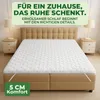A mattress topper on a bed with bedside tables and lamps in the background. Produktbild-Vorschau