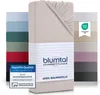 A stack of folded fitted sheets in various colors, with one sheet prominently displayed in the foreground with branding and certification labels. Voir les images du produit