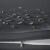 Close-up of water droplets on a dark gray fabric surface, showing the material's water-repellent properties. A zipper is visible at the bottom. Náhled obrázku produktu