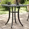 A square outdoor table with two coffee cups on it, set on a paved patio with greenery in the background. Náhľad obrázku produktu