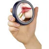 A person's hand holds a compact mirror, and the mirror reflects the person's lips as they apply red lipstick. Anteprima dell’immagine prodotto