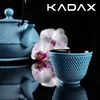 A blue cast iron teapot and cup are displayed with orchids against a black background, with the brand name KADAX at the top. Náhled obrázku produktu