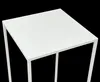A close-up view of a white, square-topped side table with a metal frame against a black background. Náhled obrázku produktu