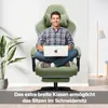 A man is sitting cross-legged on a green gaming chair with a laptop on his lap. There is a plant on the left and a floor lamp on the right. Náhľad obrázku produktu