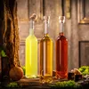 Three glass bottles filled with different colored liquids, placed on a wooden surface with moss and a piece of wood. Produktbild-Vorschau