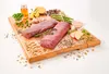 A collection of ingredients for dog food, including raw meat, vegetables, herbs, and oil, arranged on a wooden cutting board. Náhľad obrázku produktu