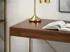 A close-up view of a wooden desk with a gold lamp and an open book. Voir les images du produit