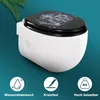 A white toilet with a black lid featuring a decorative design, set against a teal background with a palm frond in the upper left corner. Below the toilet are three circular icons with text. Produktbild-Vorschau