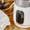 Close-up of a white electric kettle with a digital display showing the temperature, placed on a wooden surface with some tea leaves scattered around. Produktbild-Vorschau