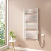 A white electric towel radiator is mounted on a light pink wall next to a window. A small white table with a plant in a white pot is placed to the left of the radiator. Voir les images du produit