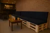 A dark blue pallet sofa with cushions and a wooden coffee table with two glasses of orange juice in front of a brick wall. Anteprima dell’immagine prodotto