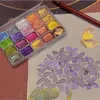 A set of watercolor paints is shown next to a drawing of a butterfly and flowers, with a pencil in the background. Voir les images du produit