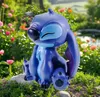 A blue Stitch figurine sitting in a garden with flowers. Produktbild-Vorschau