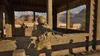 A soldier in desert camouflage holding a sniper rifle in a wooden structure with a desert landscape in the background. Produktbild-Vorschau