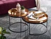 Two round nesting coffee tables with gold hammered tops and black metal legs are placed on a gray rug next to a purple sofa. Voir les images du produit