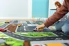 A child's hand is playing with toy cars on a play mat depicting a city street. Produktbild-Vorschau