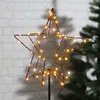A star-shaped LED light decoration is shown against a brick wall and a blurred Christmas tree. Produktbild-Vorschau
