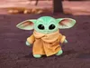 A plush toy of Baby Yoda from The Mandalorian is standing on a textured surface with a blurred background. Produktbild-Vorschau