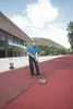 A man is pressure washing a red track surface next to a modern building. Produktbild-Vorschau