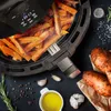 An air fryer filled with sweet potato fries, surrounded by ingredients like sweet potatoes, garlic, rosemary, and olive oil. Produktbild-Vorschau