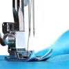 A close-up shot of a sewing machine needle and foot pressing down on blue fabric. Produktbild-Vorschau
