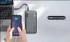 A person is holding a smartphone while a power bank is connected to a laptop and the smartphone. Produktbild-Vorschau
