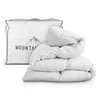 A white duvet is folded and placed next to its white storage bag, which has a mountain logo and text on it. Produktbild-Vorschau