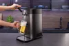 A person is pouring beer from a dispenser into a mug in a modern kitchen setting. Voir les images du produit