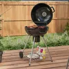 A charcoal grill with food cooking on it, set up on a wooden deck in a backyard setting. Produktbild-Vorschau