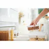 A hand is placing a clear container filled with almonds into a refrigerator or pantry. Voir les images du produit