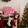 A festive Christmas scene with an advent calendar on a mantelpiece, stockings hanging below, and a decorated Christmas tree. Podgląd zdjęcia produktu