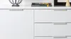 A close-up view of a white sideboard with drawers and a cabinet door. Produktbild-Vorschau