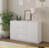 A white sideboard with drawers and doors is shown in a room with a plant and a lamp. Náhled obrázku produktu