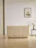 A tufted beige loveseat sits on a wooden floor in front of a white wall with a framed floral print. Produktbild-Vorschau