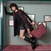 A woman poses with a handbag in a stylized room. Náhľad obrázku produktu