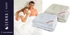 A couple is lying in bed under a duvet, with folded duvets in the foreground. Voir les images du produit