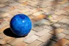 A blue ceramic garden ball rests on a brick patio. Produktbild-Vorschau