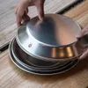 Hands stacking metal plates on a wooden table. Náhled obrázku produktu