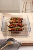 A glass baking dish filled with stuffed eggplant halves, placed on a wooden surface with a napkin and spoon in the foreground. Produktbild-Vorschau