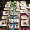 A beautifully set dining table with multiple place settings, featuring plates of food, drinks, and floral arrangements. Produktbild-Vorschau