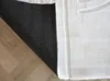 The underside of a white rug is shown, partially covering a wooden floor. Produktbild-Vorschau
