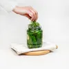 A hand is adding dill to a jar of pickles. Produktbild-Vorschau
