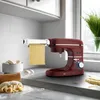 A red stand mixer with a pasta attachment is making a sheet of pasta in a kitchen setting. Anteprima dell’immagine prodotto