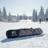 A snowboard bag lies on a snowy ski slope with snow-covered trees and a ski lift in the background. Produktbild-Vorschau