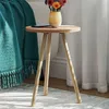 A small wooden side table with a vase of flowers and a phone on it, next to a teal blanket. Produktbild-Vorschau