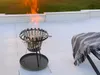 A fire pit with flames burning on a patio with a blanket on a chair. Produktbild-Vorschau