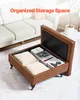 A brown leather ottoman with its lid open, revealing storage space filled with books and pillows, placed in a living room setting next to a white sofa. Anteprima dell’immagine prodotto